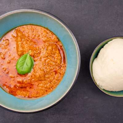 A bowl of creamy peanut sauce served alongside a portion of soft, round fufu.