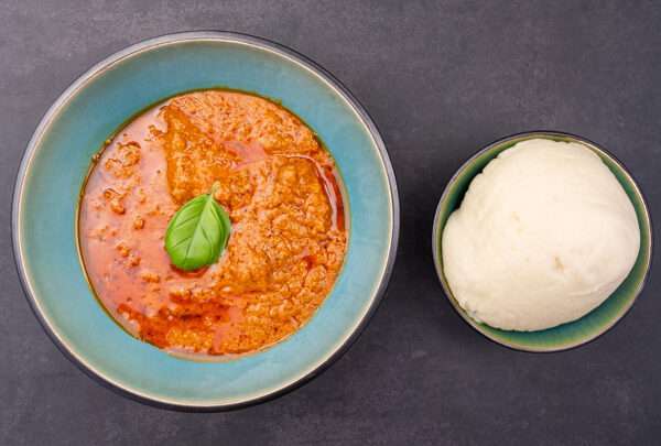 A bowl of creamy peanut sauce served alongside a portion of soft, round fufu.